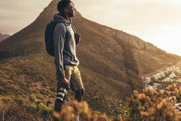 Junger Mann steht mit seiner DSLR-Kamera auf einem Bergpfad und betrachtet die Aussicht. Social-Media-Influencer auf Wandertour für neue Inhalte für seinen Kanal. - JLPSF13329