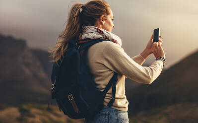Junge Frau, die mit ihrem Smartphone Bilder von einer schönen Landschaft macht. Frau, die auf einer Wandertour neue Inhalte für ihre sozialen Medien aufnimmt. - JLPSF13330