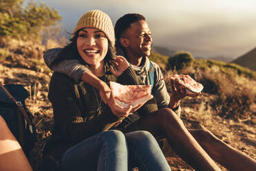 Zwei Freunde essen Pizza auf einem Bergpfad sitzend. Mann und Frau auf Wandertour essen Pizza. - JLPSF13333