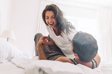 Junges Paar, das sich zu Hause auf dem Bett vergnügt. Mann liegt auf dem Bett und seine Freundin liegt oben und lächelt. - JLPSF13354