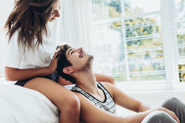 Junge Frau gibt ihrem Freund eine Kopfmassage im Schlafzimmer. Paar entspannt sich zusammen im Schlafzimmer. - JLPSF13358