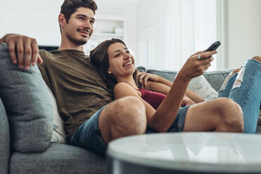 Lovely young couple relaxing at home enjoying a television program. Man and woman relaxing on sofa watching television together at home. - JLPSF13360