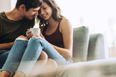 Affectionate young couple at home. Cozy and cuddly young couple sitting on sofa at home in romantic moment. - JLPSF13365