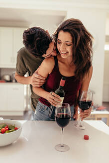 Mann steht hinter einer Frau, die in der Küche Weingläser füllt. Romantisches Paar in der Küche mit Wein. - JLPSF13379