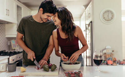 Loving young couple cutting vegetables together at kitchen counter. Young man and woman in love cooking food together at home. - JLPSF13380