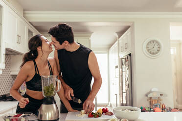 Fit young couple in love preparing healthy smoothie in kitchen. Couple about to kiss while preparing healthy breakfast in kitchen. - JLPSF13381
