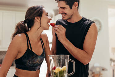 Beautiful couple preparing healthy breakfast together in kitchen. Young man feeding a strawberry to woman in kitchen. - JLPSF13382