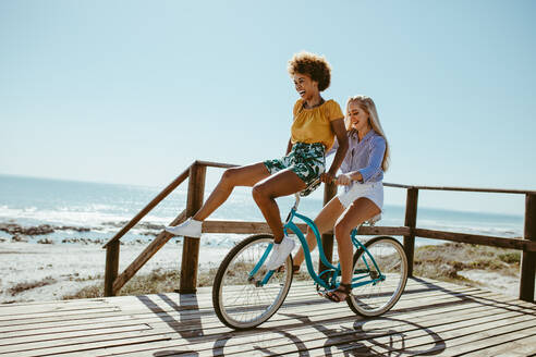 Frau auf dem Fahrrad mit ihrer Freundin auf dem Lenker sitzend. Zwei Mädchen auf einer Fahrradtour, die viel Spaß haben. - JLPSF13398
