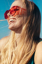 Nahaufnahme einer fröhlichen jungen Frau mit Sonnenbrille, die wegschaut und lächelt. Kaukasische Frau, die ihren Sommerurlaub genießt. - JLPSF13414