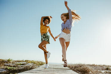 Zwei aufgeregte Freundinnen, die mit Freude auf der Strandpromenade laufen. Zwei Frauen, die sich im Urlaub amüsieren. - JLPSF13439