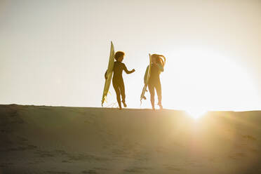 Zwei Surferinnen, die ein Surfbrett tragen und zusammen am Strand laufen. - JLPSF13441