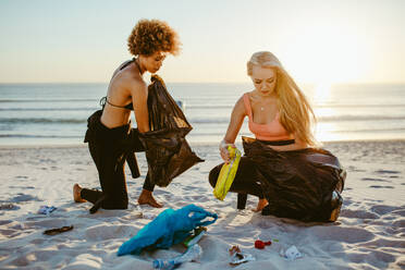 Zwei junge Frauen sammeln Müll am Strand auf. Eine Surferin säubert den Strand und sammelt die Abfälle in einem Müllsack. - JLPSF13452