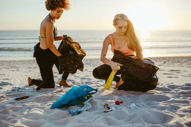 Zwei Surferinnen sammeln Müll am Strand auf. Freiwillige Frauen reinigen den Strandbereich. - JLPSF13453