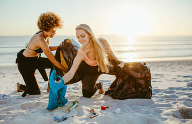 Young female surfers collecting trash in garbage bags from the beach. Women cleaning up a sandy seashore area. - JLPSF13455