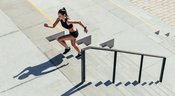 Sportswoman running up the steps as a part of workout routine. Female in sportswear exercising on staircase outdoors. - JLPSF13491