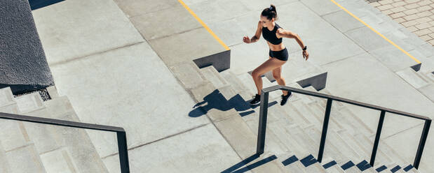 Junge Frau, die die Treppe hinaufläuft, um zu trainieren. Sportler in Sportkleidung, der auf einer Treppe im Freien trainiert. - JLPSF13492