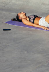 Young woman lying with her eyes closed on yoga mat. Fitness female resting after training session. - JLPSF13511