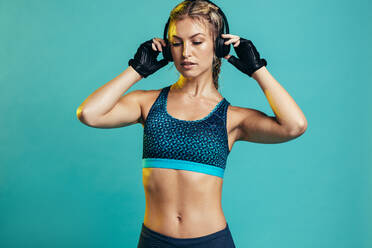 Muscular female with headphones on blue background. Fitness woman relaxing and listening music during her workout - JLPSF13522