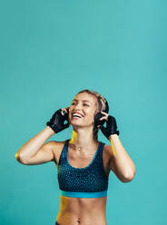 Smiling woman with headphones resting after workout. Fit female athlete taking a break after exercising. - JLPSF13524