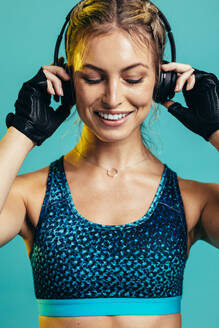 Young female athlete with headphones on blue background. Fitness woman relaxing and listening music after workout. - JLPSF13525