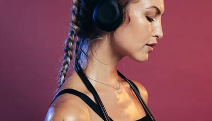 Close up of woman wearing headphones with skipping ropes around her neck. Female athlete resting after exercising. - JLPSF13538