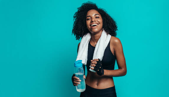 Happy young woman resting after workout on blue background. Healthy young female taking a break after exercising. - JLPSF13585