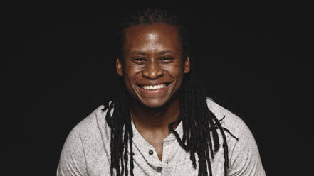 Fröhlicher afrikanischer Mann mit langen Dreadlocks isoliert auf schwarzem Hintergrund. Portrait eines lächelnden Mannes, der in die Kamera schaut. - JLPSF13643