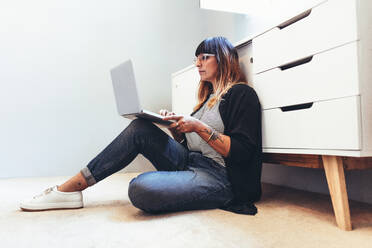 Freelance woman working on laptop computer sitting on floor. Female entrepreneur sitting down on the floor working from home. - JLPSF13656