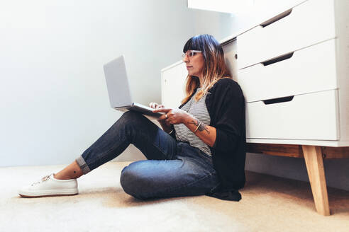 Freiberufliche Frau arbeitet am Laptop auf dem Boden sitzend. Unternehmerin sitzt auf dem Boden und arbeitet von zu Hause aus. - JLPSF13656