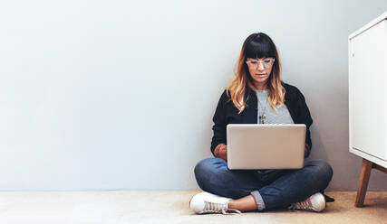 Female freelancer working on laptop sitting on floor. Woman using a laptop computer working from home. - JLPSF13657