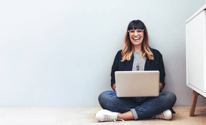 Lächelnde Frau, die zu Hause auf dem Boden sitzt und einen Laptop-Computer benutzt. - JLPSF13658