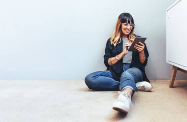 Lächelnde Frau, die auf dem Boden sitzt und einen Tablet-PC benutzt. Entspannte Geschäftsfrau, die ihre Mails auf einem Tablet-PC überprüft. - JLPSF13661