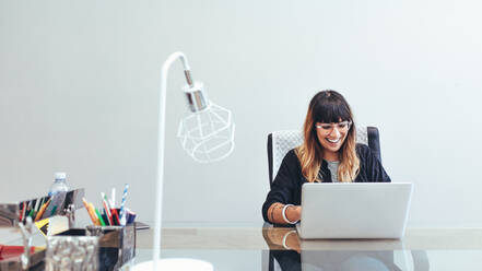 Smiling creative artist sitting at her desk in office working on a laptop. Illustrator sitting in office working on laptop. - JLPSF13662