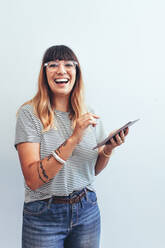 Porträt einer Geschäftsfrau, die im Büro steht und einen Tablet-PC hält. Lächelnde Frau in Jeans und T-Shirt, die einen Tablet-PC im Büro benutzt. - JLPSF13674