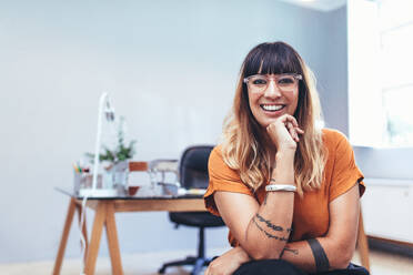 Nahaufnahme einer lächelnden Unternehmerin, die in ihrer Kabine im Büro sitzt. Lächelnde Geschäftsfrau, die im Büro sitzt und ihr Kinn auf die Hand stützt. - JLPSF13693