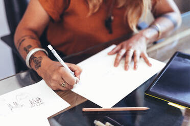 Close up of hands of an artist making a drawing on a paper. Cropped shot of a female artist making a design on a drawing paper. - JLPSF13696