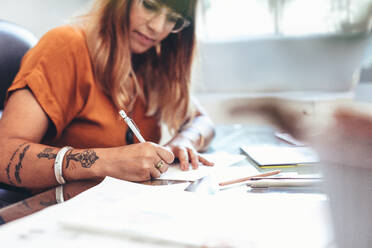 Cropped shot of a female artist making a sketch on a paper. Side view of an illustrator making a creative art sitting at her desk in office. - JLPSF13698