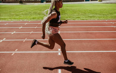 Weibliche Athletin beim Sprint auf einer Laufbahn in einem Stadion. Afrikanische Läuferin beim Training auf einer Laufbahn. - JLPSF13716