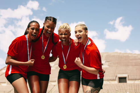 Frauenfußballmannschaft feiert den Sieg im Stadion. Fußballspielerinnen mit Medaillen schreien vor Freude nach dem Gewinn der Meisterschaft. - JLPSF13734