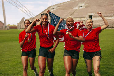 Fußballspielerinnen rennen auf dem Feld und schreien vor Freude, nachdem sie die Meisterschaft gewonnen haben. Amerikanische Frauenfußballmannschaft feiert die Meisterschaft, schreit vor Freude und rennt auf dem Feld und hält die Nationalflagge. - JLPSF13737