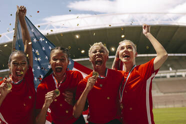 Amerikanische Frauen-Fußballmannschaft feiert Meisterschaft. Frauen-Fußballmannschaft schreit auf dem Feld hält nationale Flagge mit Konfetti fallen um. - JLPSF13739