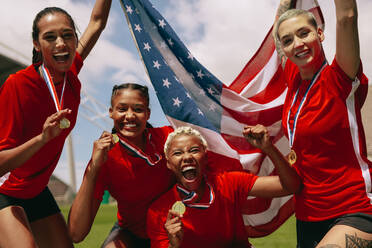 Gruppe von weiblichen Fußballmannschaft mit Medaillen halten US-Nationalflagge auf dem Feld. Frau Fußballmannschaft feiert Meisterschaft Sieg. - JLPSF13740