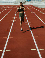 Weibliche Athletin beim Sprint auf einer Laufbahn in einem Leichtathletikstadion. Läuferin beim Training auf einer Laufbahn. - JLPSF13759