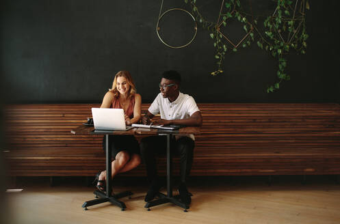 Geschäftspartner in einem Café, die an einem Laptop arbeiten. Freunde, die mit Laptop und Notizblöcken an einem Kaffeetisch sitzen und arbeiten. - JLPSF13779