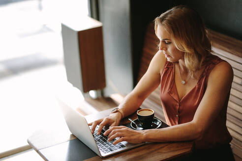 Freiberufler sitzt an einem Kaffeetisch und arbeitet am Laptop mit einer Tasse Kaffee auf dem Tisch. Frau bei der Arbeit in einem Café. - JLPSF13783