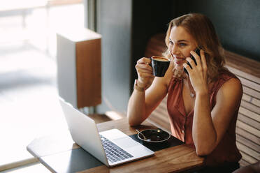 Freiberufler sitzt in einem Café mit einem Laptop auf dem Tisch, während über Handy sprechen. Frau tut ihre Arbeit in einem Café sitzen, während eine Tasse Kaffee trinken. - JLPSF13785