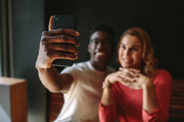 Lächelndes Paar, das ein Selfie mit dem Mobiltelefon macht. Mann und Frau teilen glückliche Momente in einem Café. - JLPSF13795