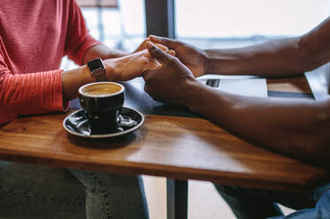 Man and woman sitting at a coffee table holding hands with a cup of coffee on the table. Cropped image of a man holding hands of a woman at a coffee shop. - JLPSF13798