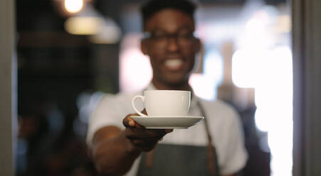 Closeup of barista offering a coffee cup. Coffee shop owner serving coffee. - JLPSF13802
