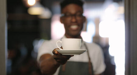 Nahaufnahme eines Barista, der eine Tasse Kaffee anbietet, und eines Kaffeehausbesitzers, der Kaffee serviert. - JLPSF13802